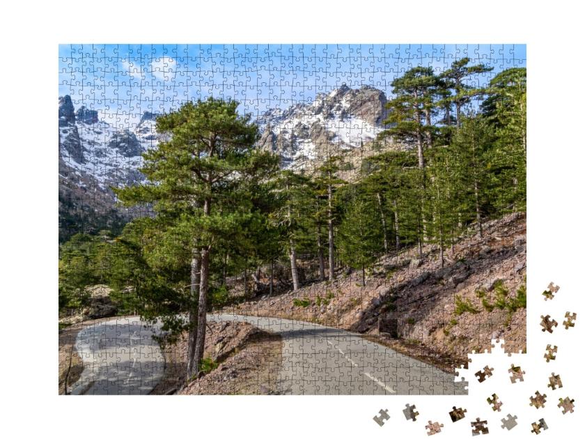 Puzzle de 1000 pièces « Route sinueuse à travers une forêt de pins devant une chaîne de montagnes enneigées »