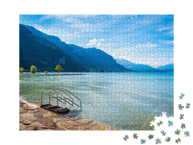 Puzzle de 1000 pièces « Vue panoramique sur le lac d'Annecy et ses montagnes avec un ciel bleu et quelques nuages le matin »